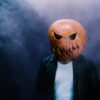 a person wearing a pumpkin mask on a dark background