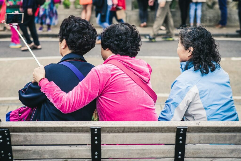 three person taking selfie while sitting on a bench during day time