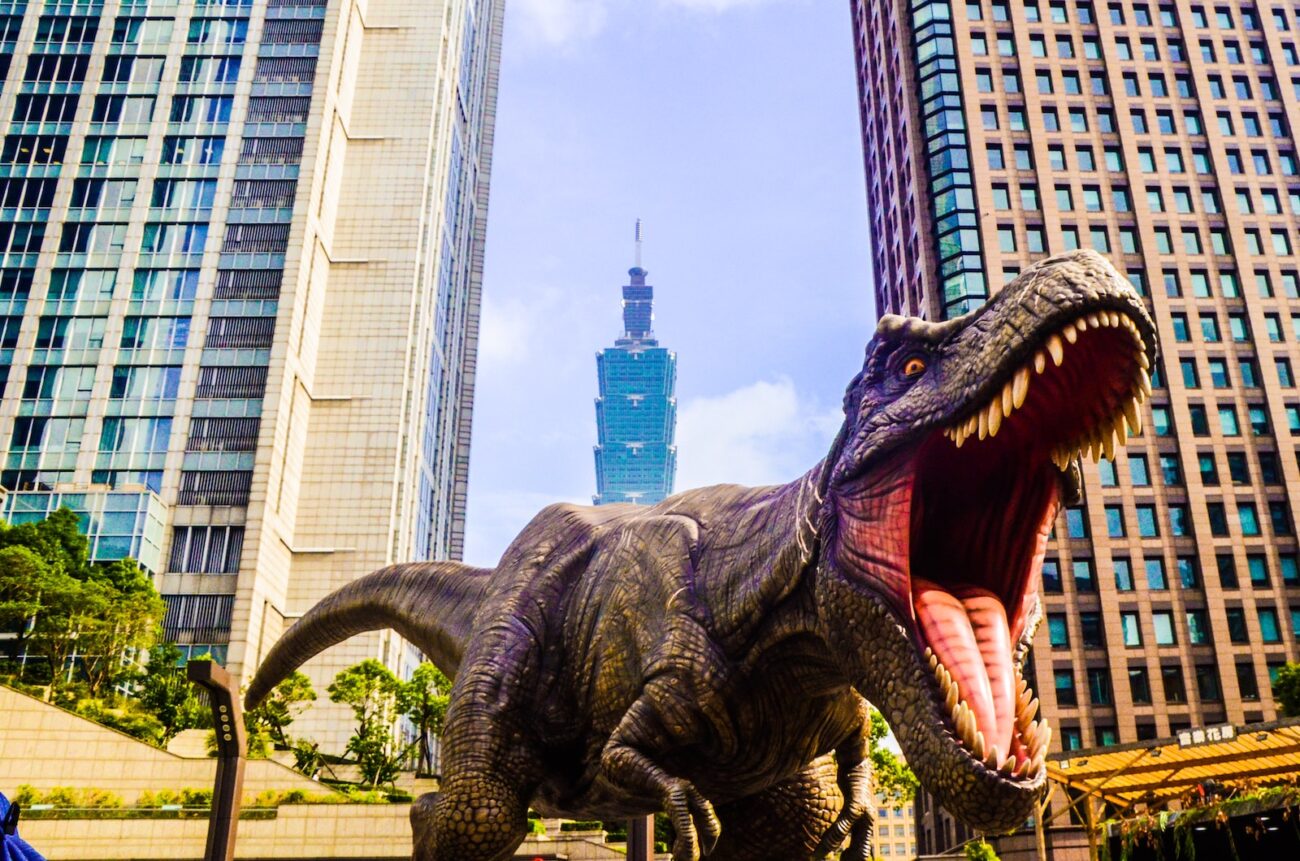 dinosaur with open mouth beside buildings still selective focus photography of