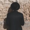 a man wearing a black hat standing in front of a stone wall