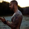 topless man with body tattoo standing on water during daytime