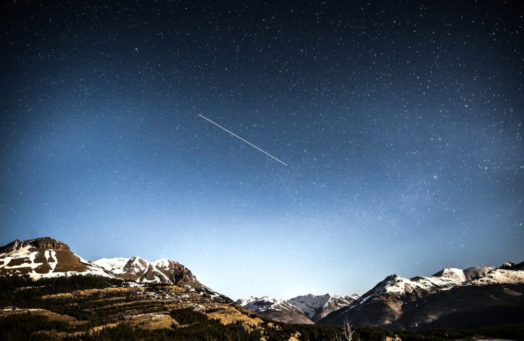 photo of shooting star over snow covered mountains