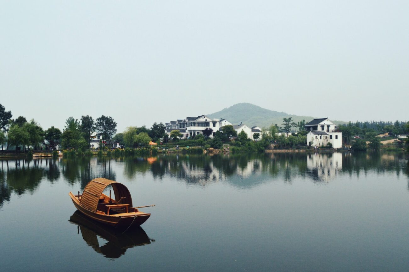 brown wooden boat on body of water overlooking houses by the shore at daytime