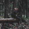 person wearing black jacket on log wod inside the forest