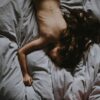 naked woman lying on gray bedspread
