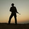 a silhouette of a man holding a rifle in the desert
